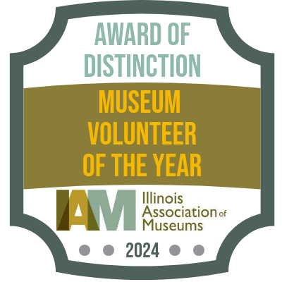 green ribbon and gray circle website badge recognizing Illinois Association of Museum's 2024 Museum Volunteer of the Year