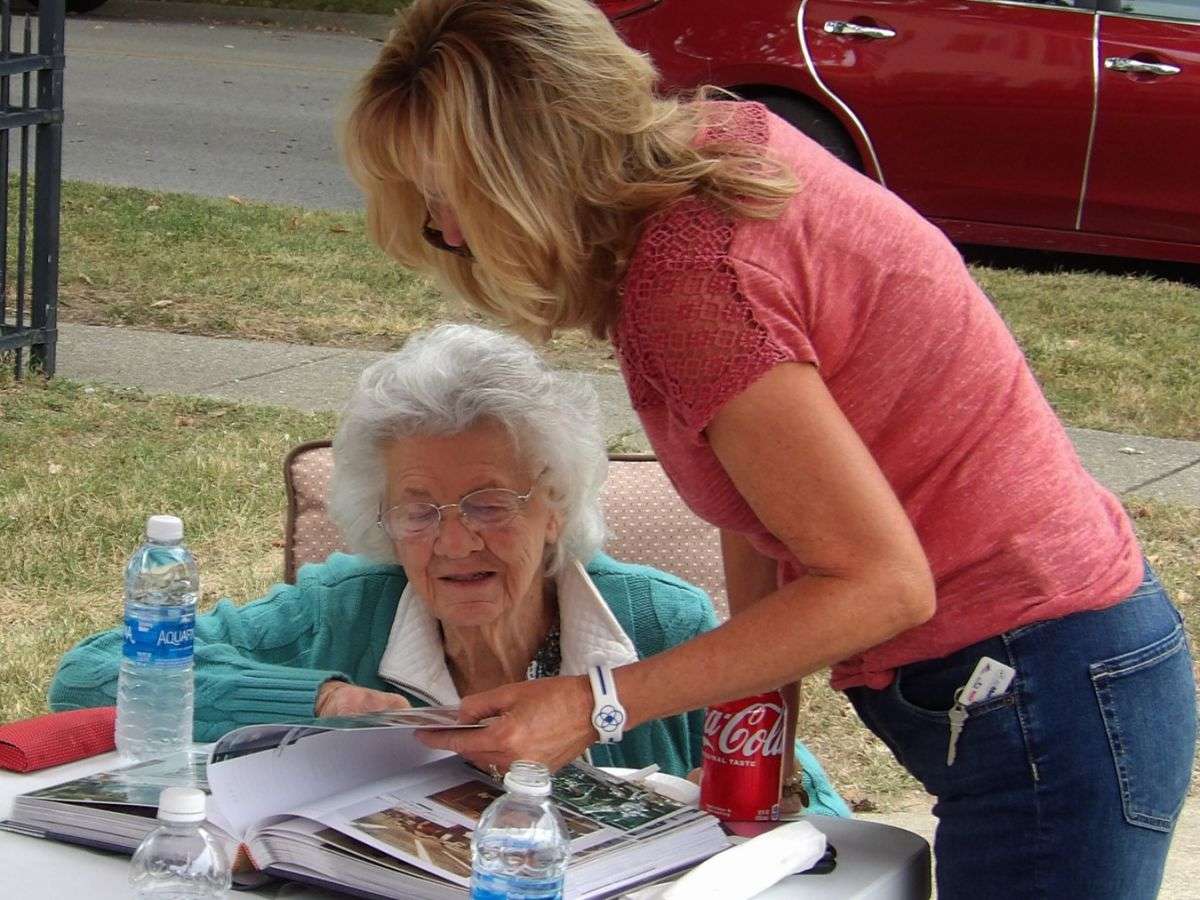 white haired older woman looks thorugh photo scrapbook with younger blonde woman